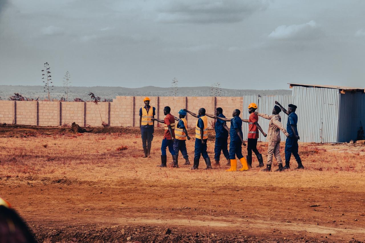A line of mine workers walking together across a fenced site.