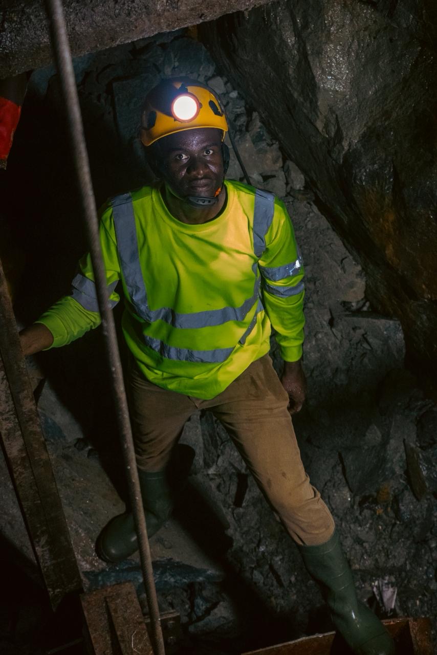 A miner looking up from a mine shaft, lit by a headlamp.