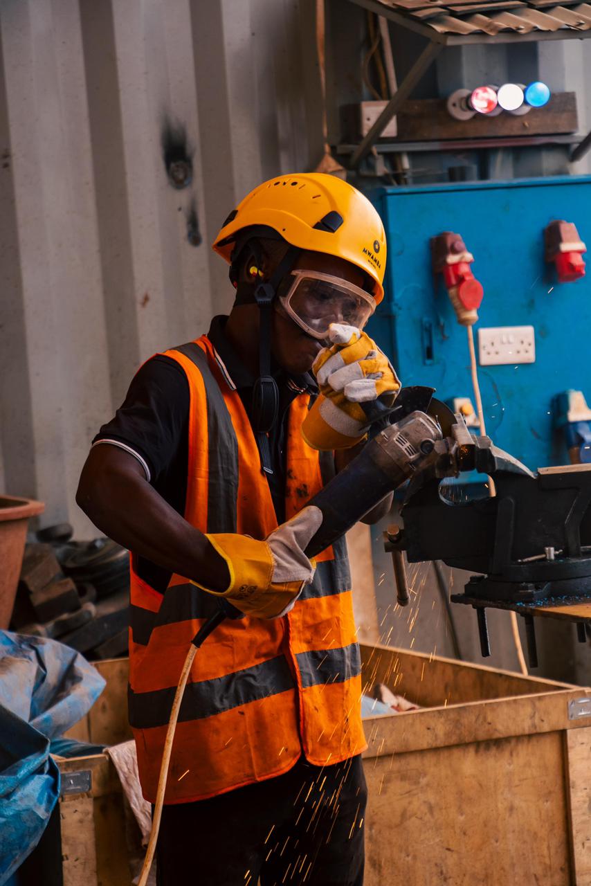 A worker using an angle grinder at a workshop bench, sparks flying.