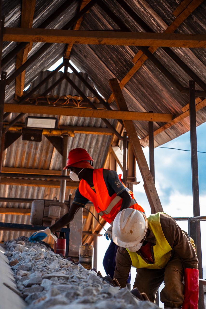 Workers hand-sorting ore on a picking line under a timber shelter.