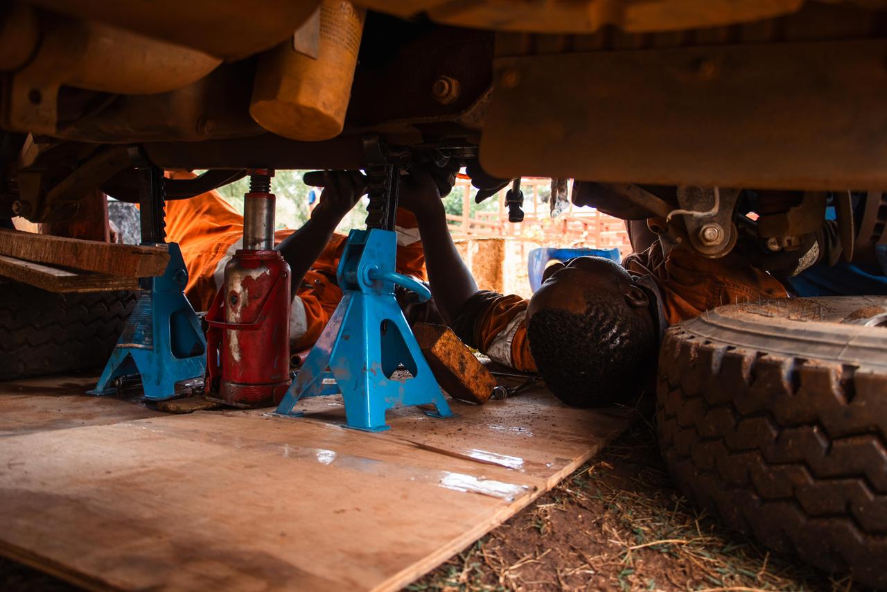 A mechanic working underneath a vehicle raised on axle stands.