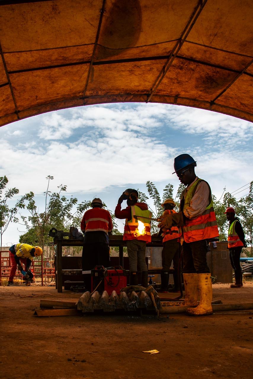 Mine workers in hi-vis pouring molten gold into moulds under a canopy.