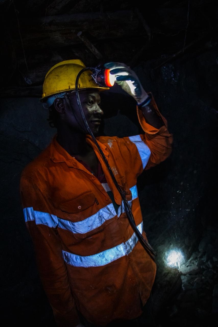 A miner in orange overalls adjusting a headlamp underground.