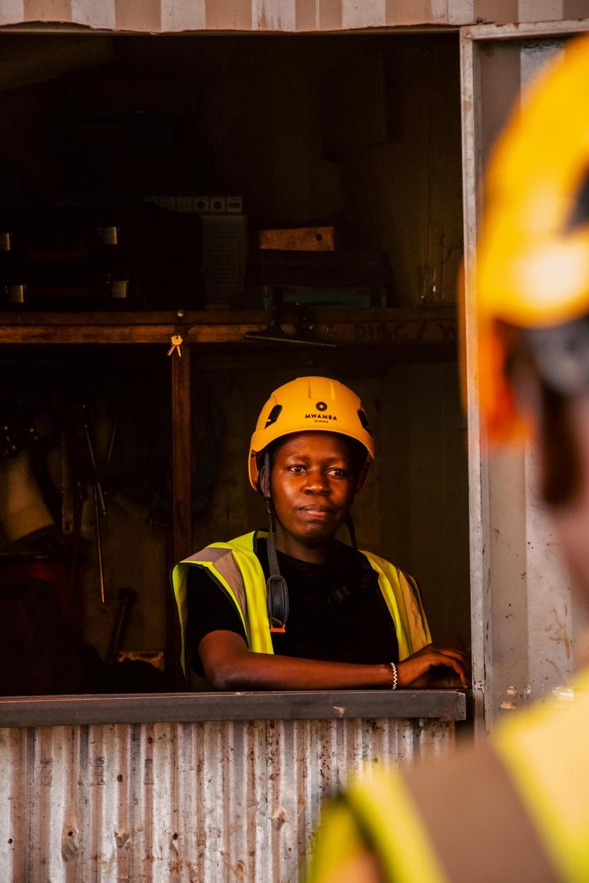 A miner in a Mwamba Mining hard hat and hi-vis vest at a mine-site office.