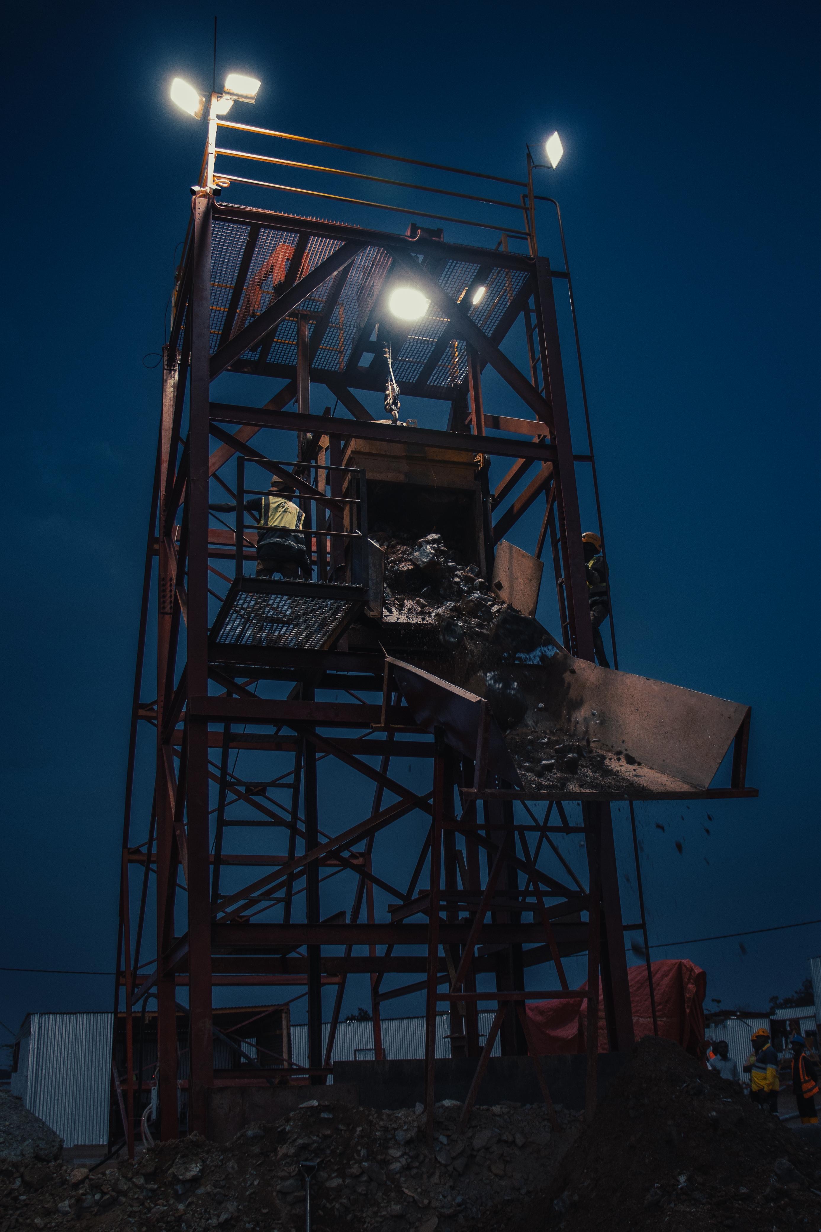 A floodlit red headframe discharging ore at night.