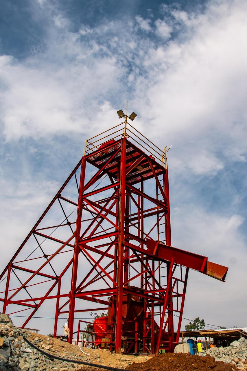 A red steel headframe rising over an artisanal mine shaft.